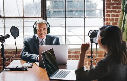 Deux présentateurs parlant devant des ordinateurs portables et des microphones