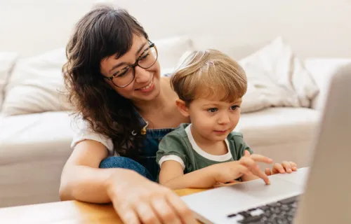 A child sitting on a woman's lap using a laptop