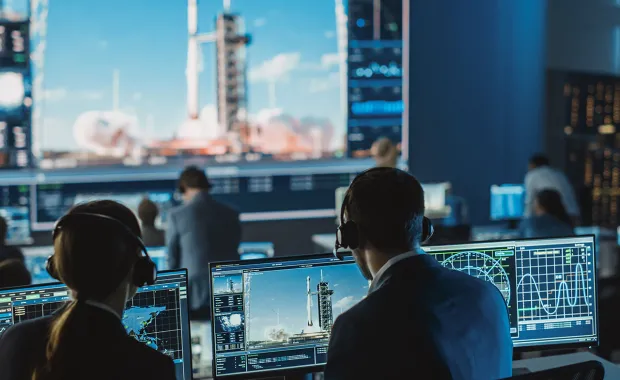 two people watching a launch in front of monitors in mission control room