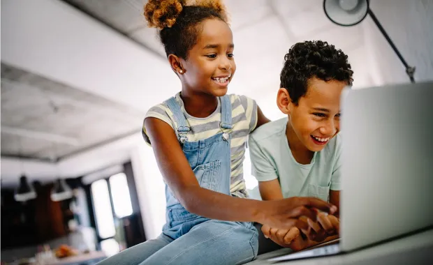 Två barn sitter skrattande tillsammans och tittar på en laptopskärm