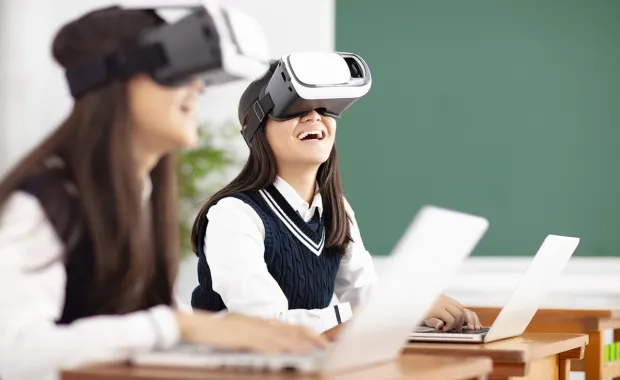 Två tjejer i skoluniform sitter skrattande med VR-glasögon