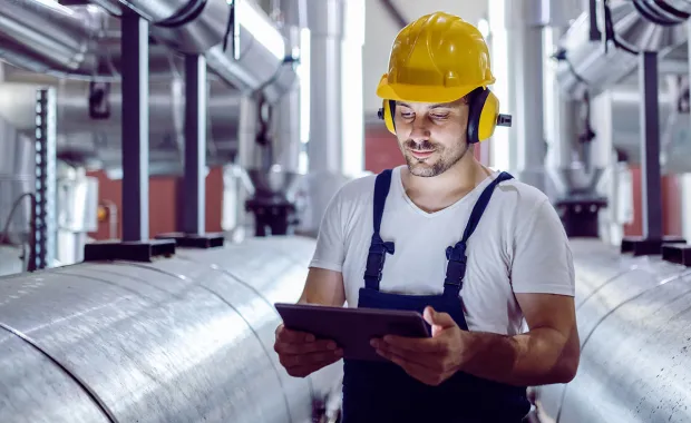 focused plant worker in a hard hat uses a tablet to check nearby machines