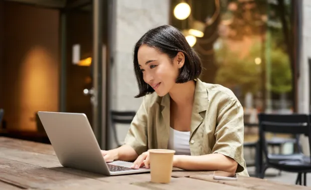 Junge Frau sitzt in einem Café und arbeitet an ihrem Laptop