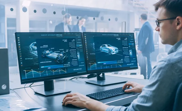 Male data scientist looking at two computer screens car factory