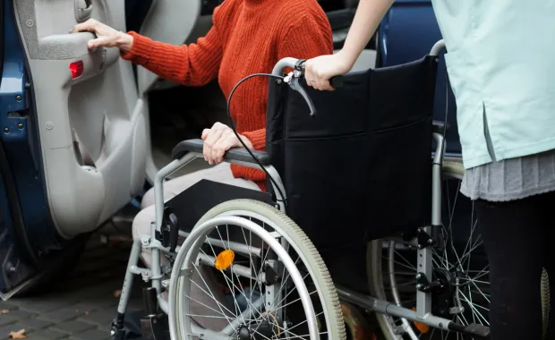 En dame som er på vei ut av en bil og over i en rullestol