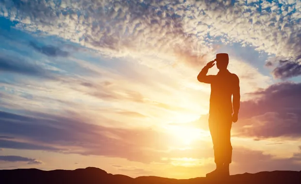 saluting soldier silhouetted in sunrise