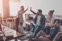 En grupp av både kvinnor och män har vänt sina kontorsstolar mot varandra i ett tomt kontorslandskap och två av männen står upp och gör en high-five