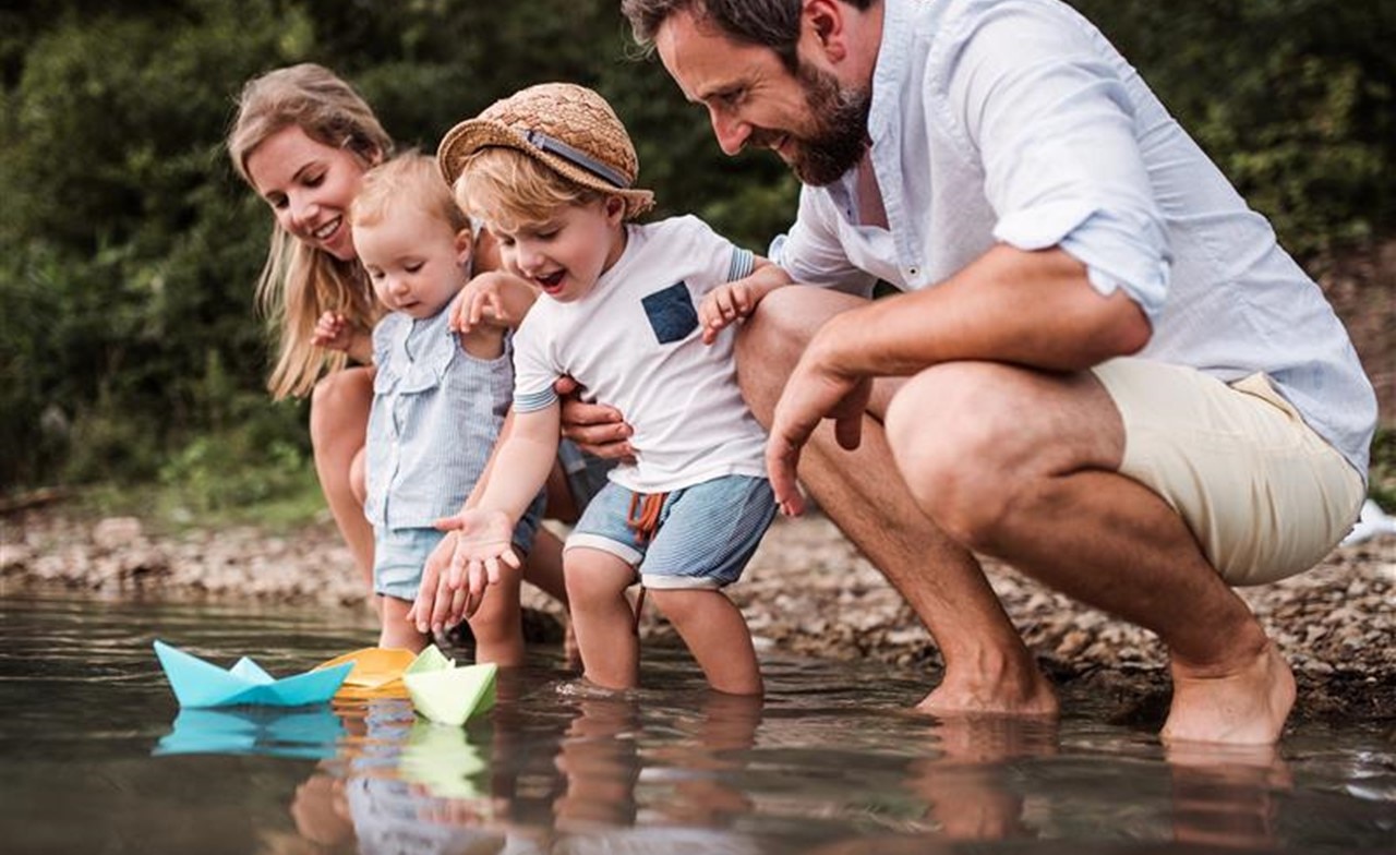 young-family-floating-paper-boats-riverbank A young family floating paper boats on a riverbank